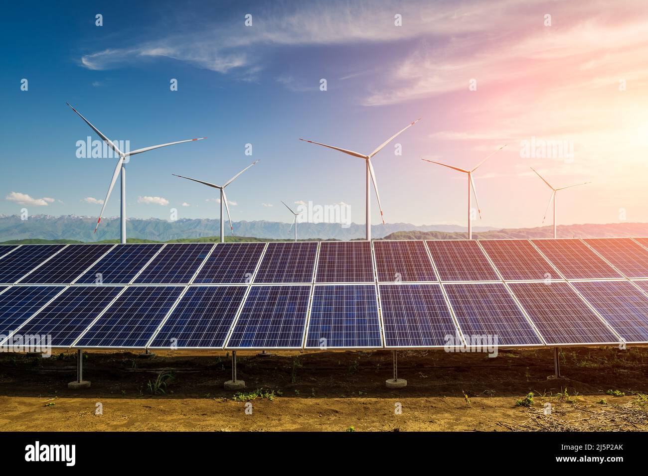 Sonnenkollektoren und Windkraftanlagen mit Berglandschaft bei Sonnenuntergang. Konzept für grüne Energie. Stockfoto