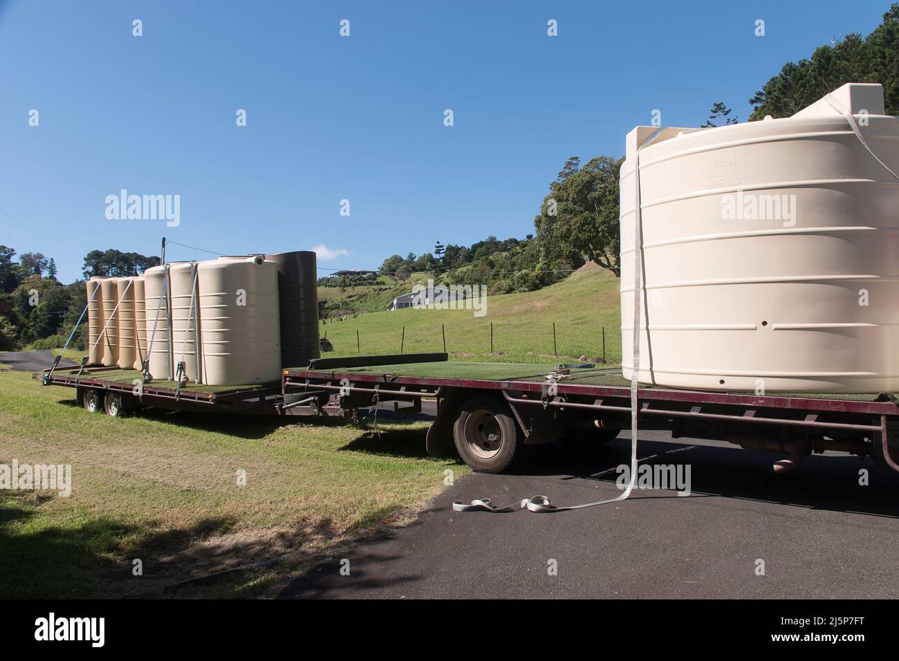 Tieflader-LKW und Anhänger liefern an einem sonnigen Tag in Queensland, Australien, Polyregenwassertanks. Geparkt auf einer schmalen Landstraße. Stockfoto