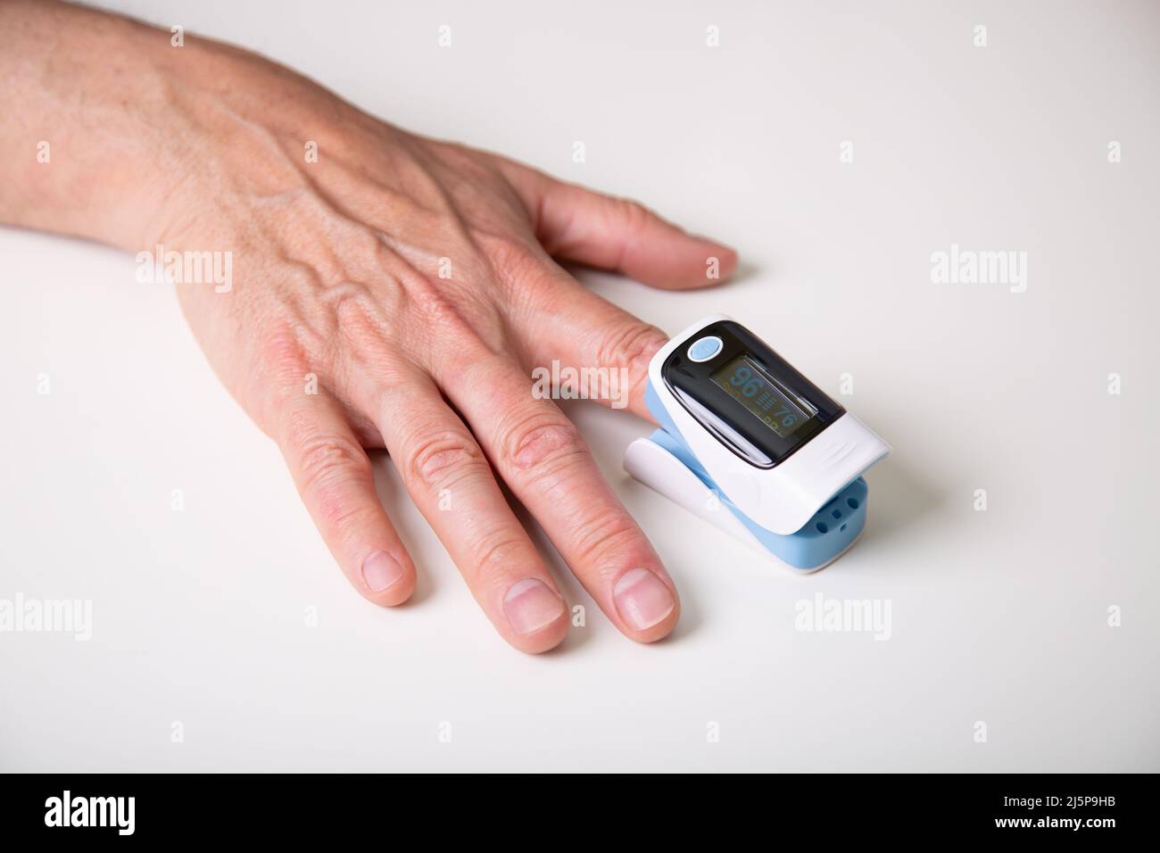 Mann mittleren Alters, der die Sauerstoffsättigung des Blutes mit einem digitalen Oximeter zu Hause misst. Stockfoto