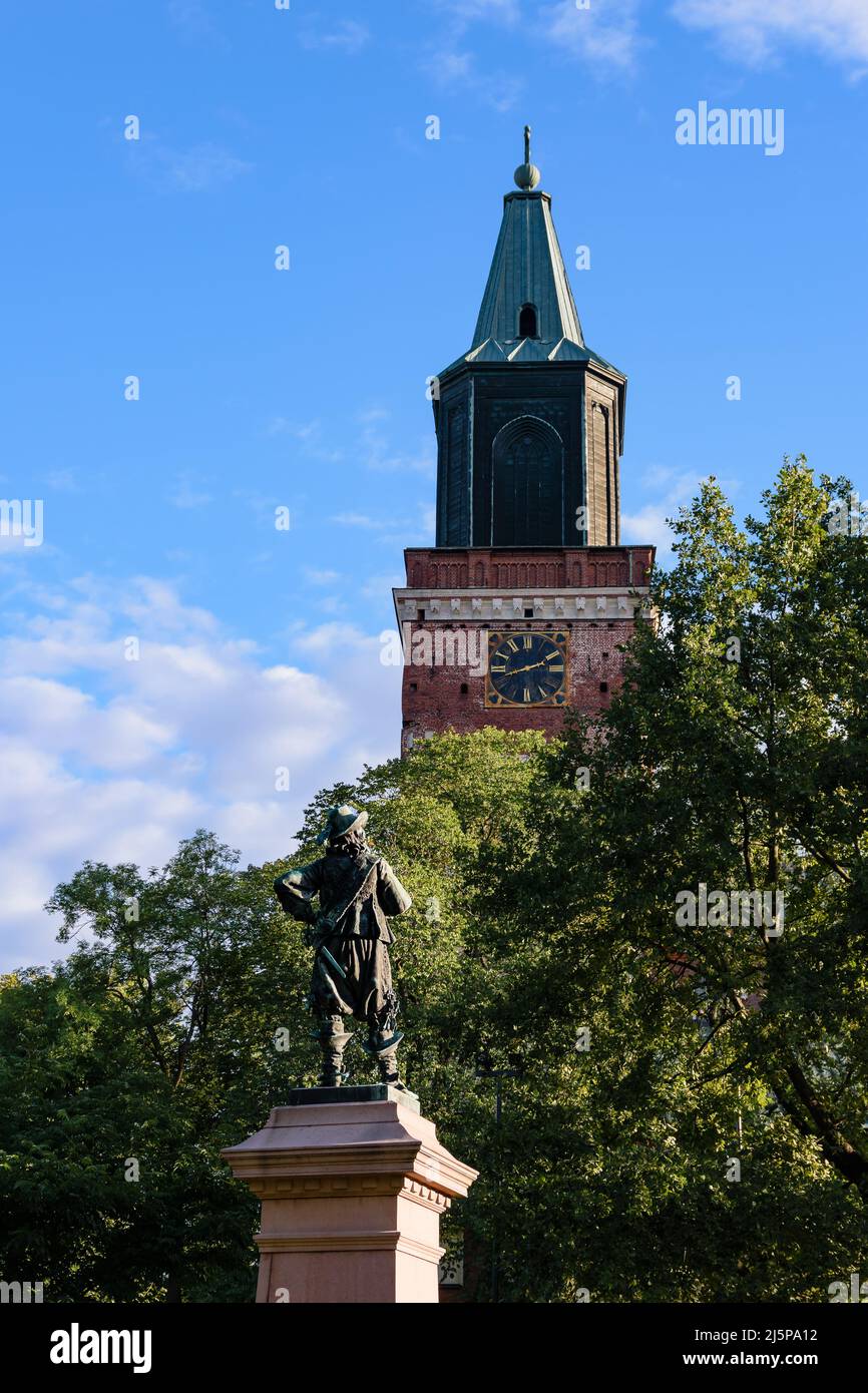 Der Turm der Kathedrale von Turku, die mittelalterliche Basilika in Finnland gegen den blauen Himmel im Sommer mit den Bäumen und die per Brahe-Statue im Vordergrund Stockfoto
