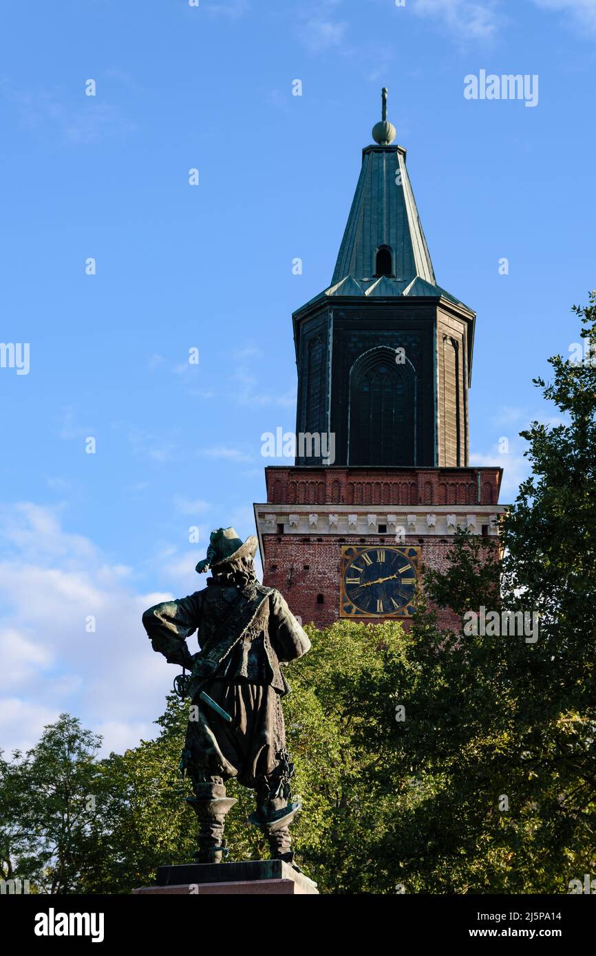 Der Turm der Kathedrale von Turku, die mittelalterliche Basilika in Finnland gegen den blauen Himmel im Sommer mit den Bäumen und die per Brahe-Statue im Vordergrund Stockfoto