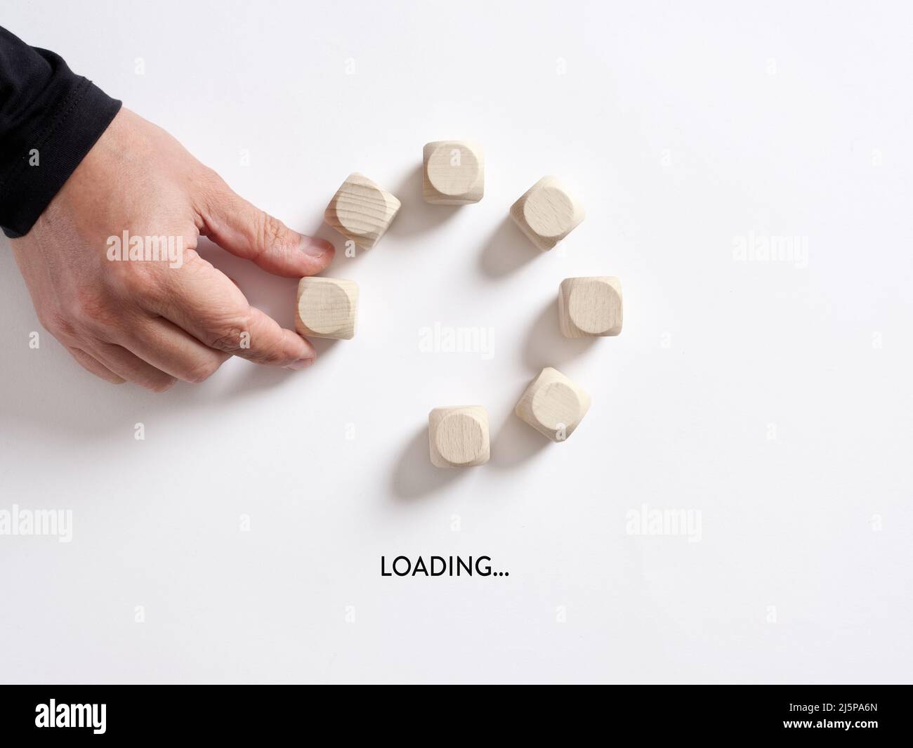 Hand platziert einen Holzwürfel in der Fortschrittsanzeige des Ladevorgangs mit dem Wort Loading. Stockfoto