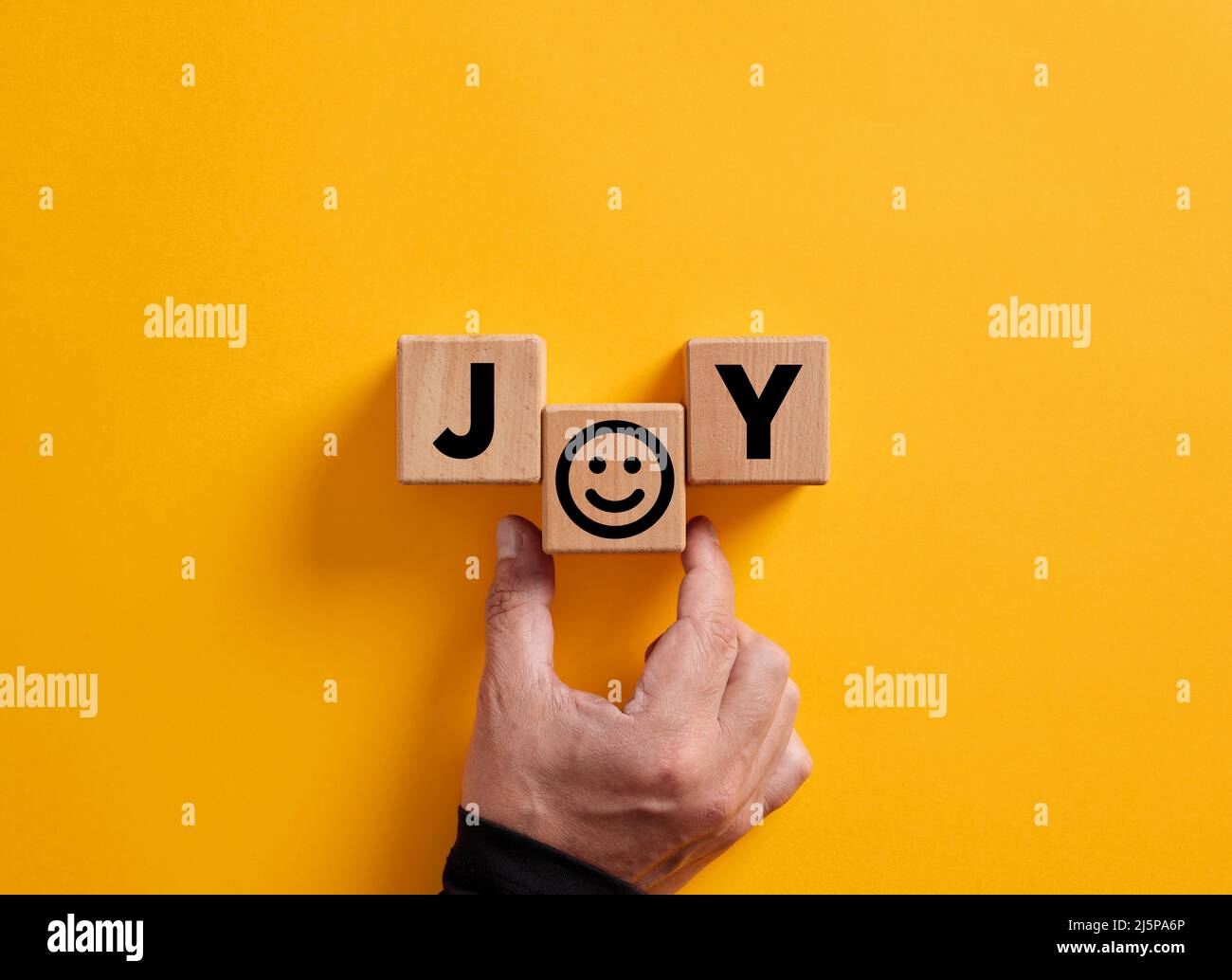 Hand legt das Wort Freude auf Holzblöcke mit einem lächelnden Gesichts-Symbol. Freude, Glück, Vergnügen, freudige Emotionen. Stockfoto