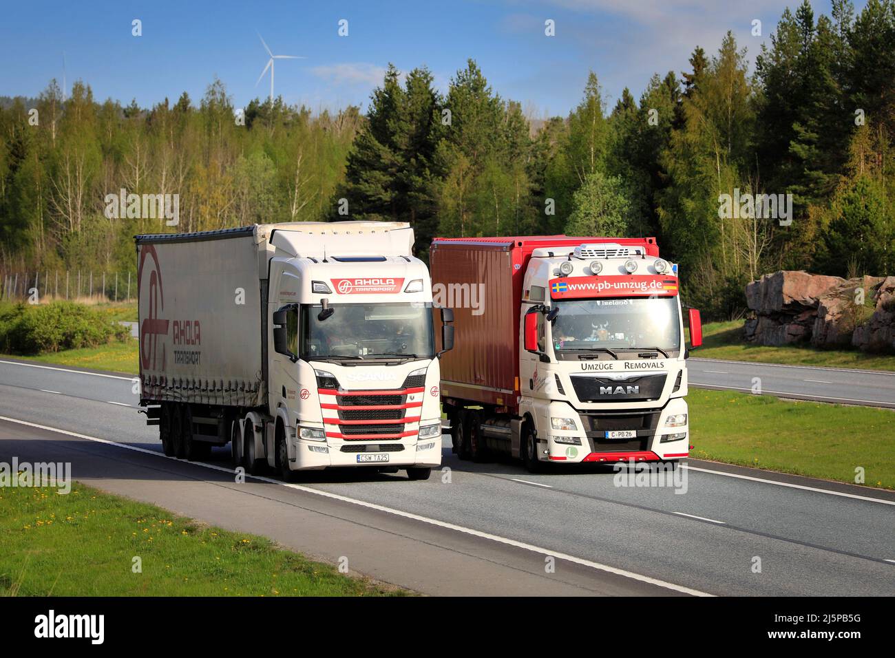 An einem sonnigen Frühlingsmorgen überholt der rot-weiße MAN-Sattelschlepper Scania-Lastwagen bergauf auf die Autobahn. Salo, Finnland. 14.Mai 2021. Stockfoto