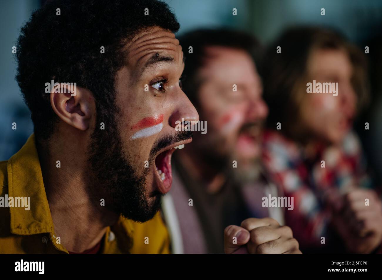 Nahaufnahme eines begeisterten Fußballfans, der ein Spiel mit Freunden zu Hause beobachtet. Stockfoto