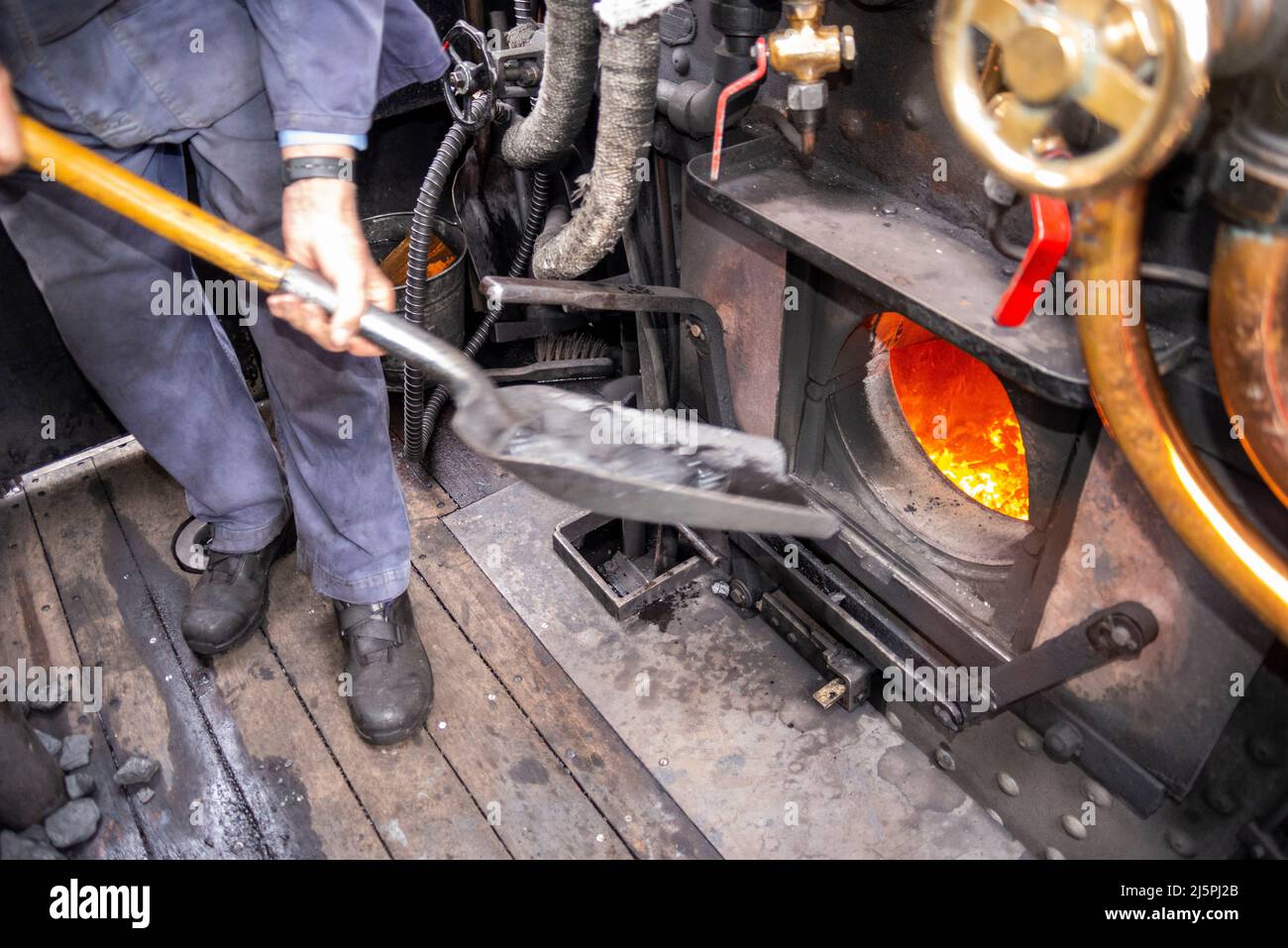 Kent & East Sussex Railway, Tenterden, Kent, Großbritannien. 25. April 2022. Die Zukunft des historischen Dampfsektors im Vereinigten Königreich ist durch die Schließung der Kohlebergwerke des Landes gefährdet, insbesondere der Trockendampfkohle, die in einer Mine in Wales ausschließlich abgebaut wird. Trockene Dampfkohle ist ein halbrauchfreier Brennstoff, der sauberer als Hauskohle verbrennt und in Dampfeisenbahnmaschinen, Zugmaschinen und dampfbetriebenen Schiffen verwendet wird. Importierte Kohle verursacht höhere Umweltbelastungen und wirkt sich durch den Transport aus Kasachstan und Kolumbien auf die Umwelt aus. Es wurde eine Veranstaltung durchgeführt, um das Problem hervorzuheben. Schaufeln von Kohle in eine Feuerstelle Stockfoto