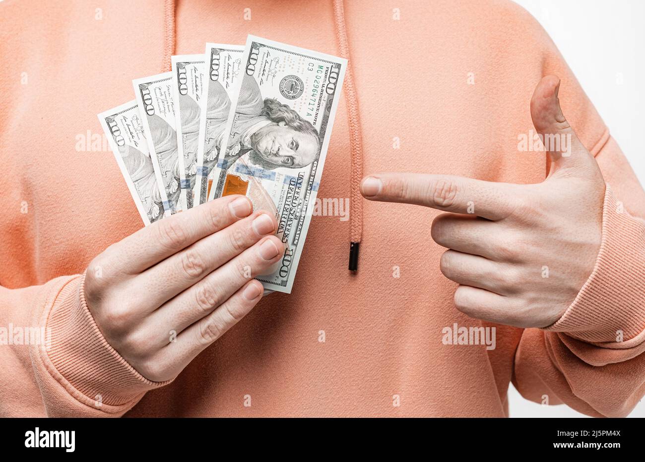 Mann, der Geld in der Dollar-Währung in den Händen hält. Kerl haben Bargeld in einem rosa oder orange Sweatshirt. Das Konzept von Geld, Gehalt, Finanzen, Investitionen Stockfoto
