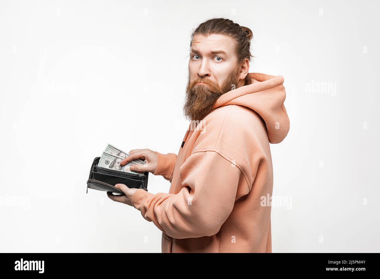 Handsom Mann hält Papier Währung in der Brieftasche und ist unglücklich auf grauem Hintergrund. Hand ziehen 100-Dollar-Banknoten aus der Brieftasche. Mann hat Bargeld. Der Nachteil Stockfoto