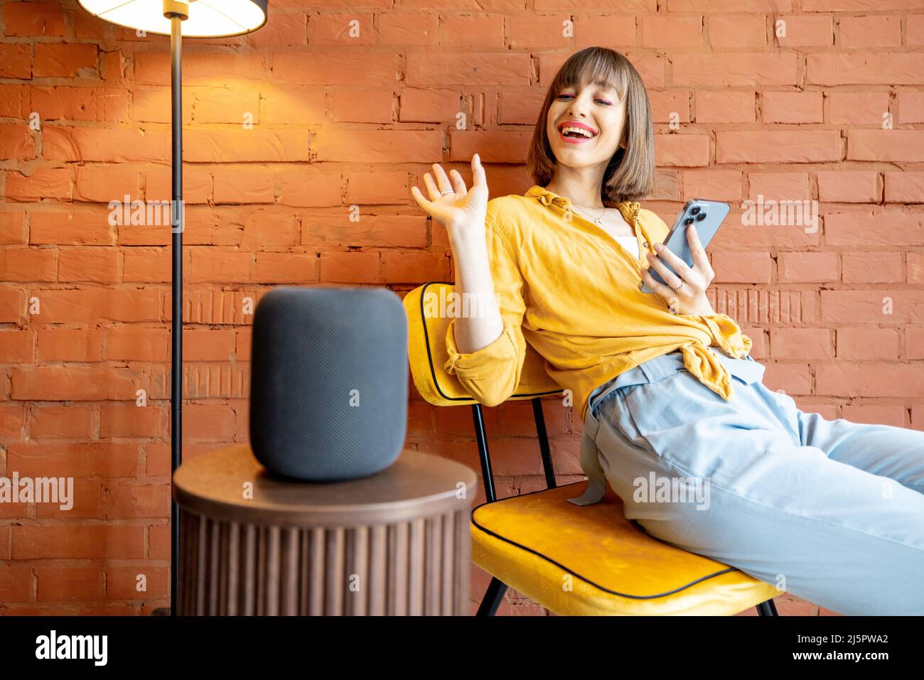 Frau mit Smart-Lautsprecher und Telefon zu Hause Stockfoto