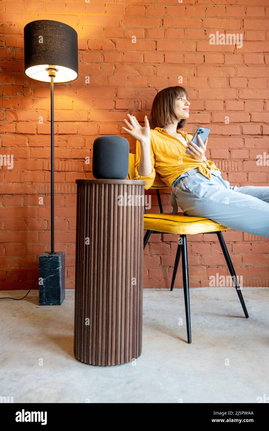 Frau mit Smart-Lautsprecher und Telefon zu Hause Stockfoto