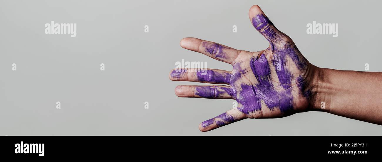 Nahaufnahme der Hand eines Mannes mit violetten Farbflecken, auf grauem Hintergrund, in einem Panorama-Format zur Verwendung als Webbanner oder Header Stockfoto
