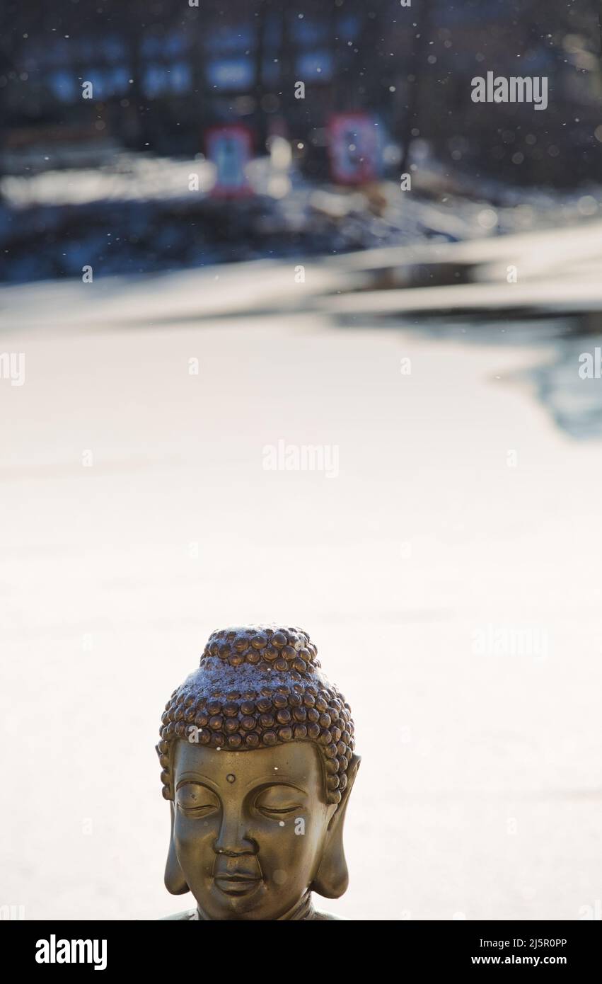 Buddha Kopf im Freien im fallenden Schnee, Schweden. Konzept von Ruhe, Spiritualität, Harmonie und Frieden Stockfoto