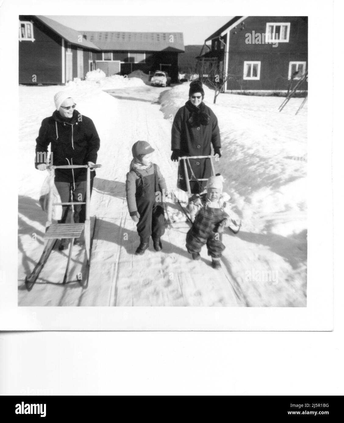 60iger Jahre authentisches Vintage-Foto von zwei Müttern mit kleinen Kindern, die Schlitten durch den Schnee schieben, Schweden Stockfoto