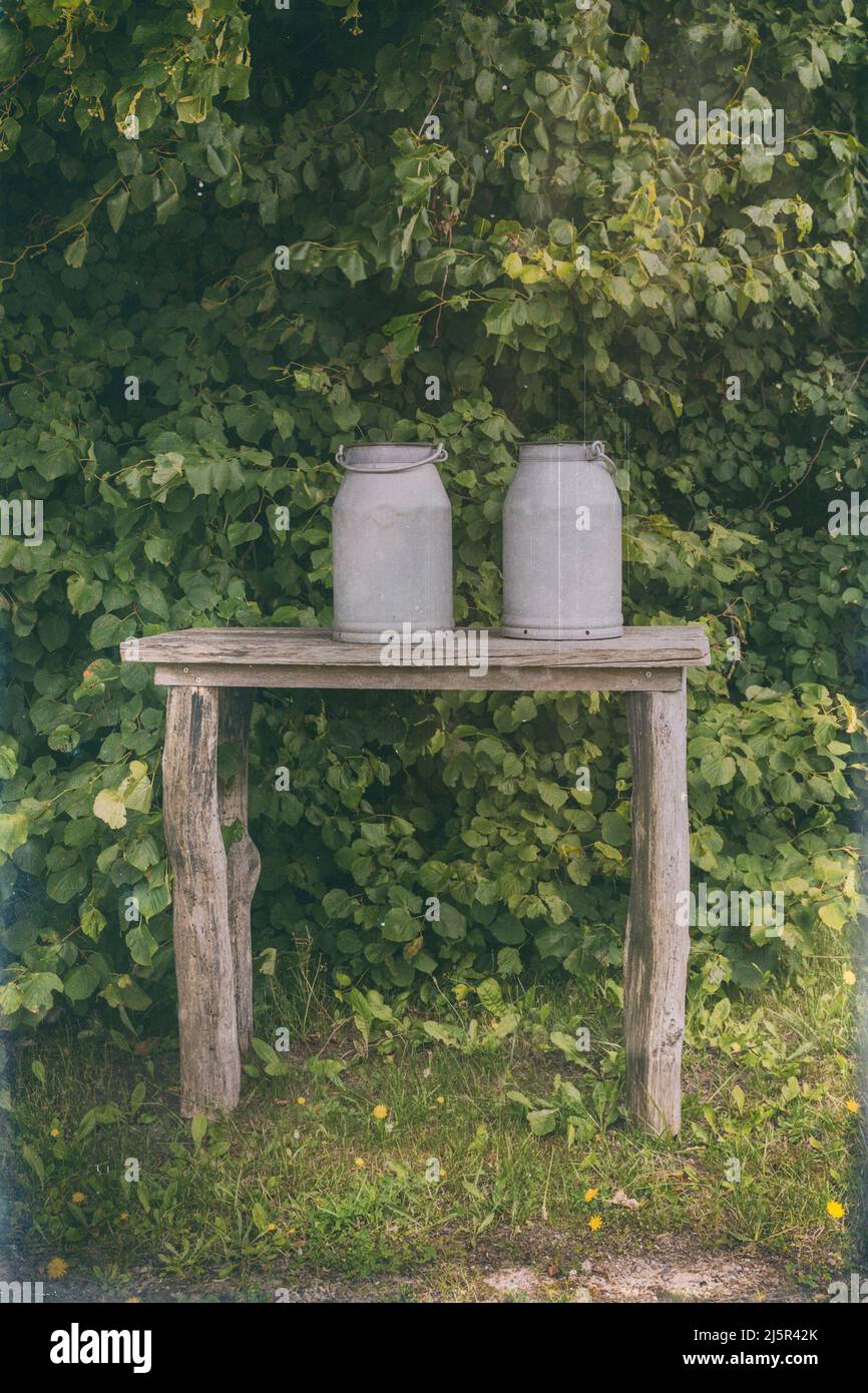 Zwei alte Milchschürfen auf Holzregalen im Freien. Bildverarbeitung im Vintage-Stil. Stockfoto