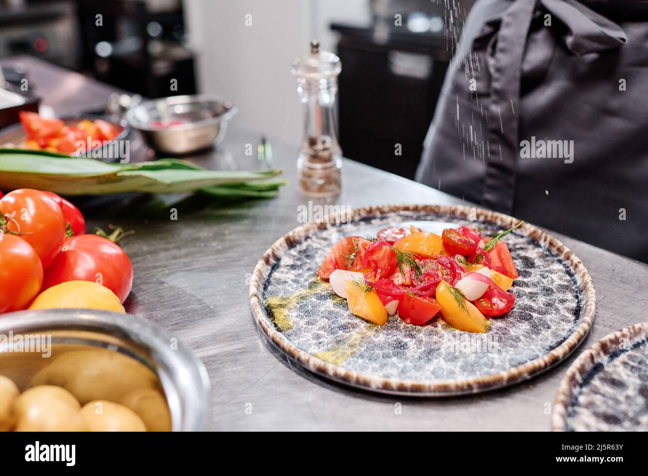 Nahaufnahme des Gerichts mit frischem Gemüsesalat auf dem Teller auf dem Tisch, wobei der Koch Gewürze hinzufügte Stockfoto