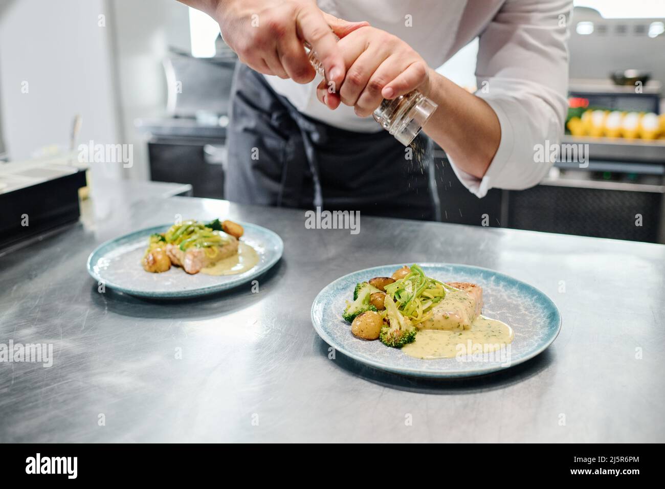 Nahaufnahme des Küchenchefs, der vor dem Servieren Gewürze aus dem Shaker auf Fertiggerichte auf den Tisch gegeben hat Stockfoto