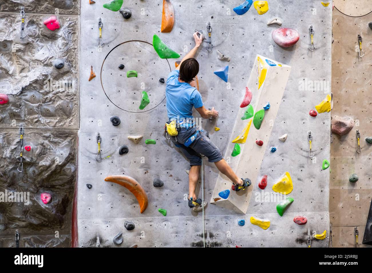 Der Kletterer trainiert an der künstlichen Felswand mit Versicherung in der Boulderhalle, April 2022, Prag, Tschechische Republik. Stockfoto
