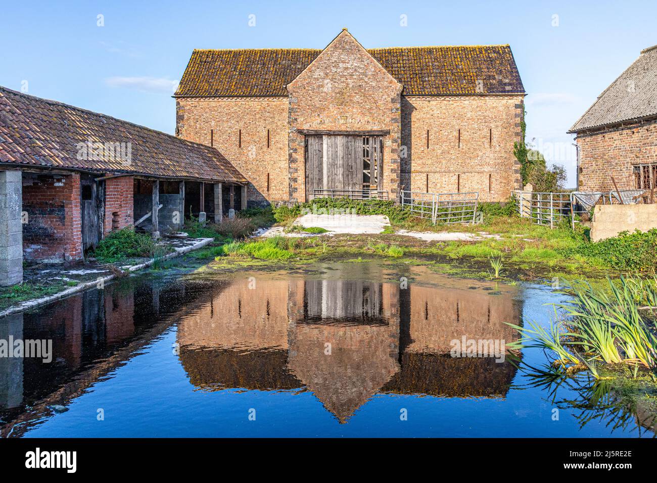 Eine alte Backsteinscheune, die sich in einer großen Pfütze im Dorf Arlingham in Gloucestershire, England, wiederspiegelt Stockfoto