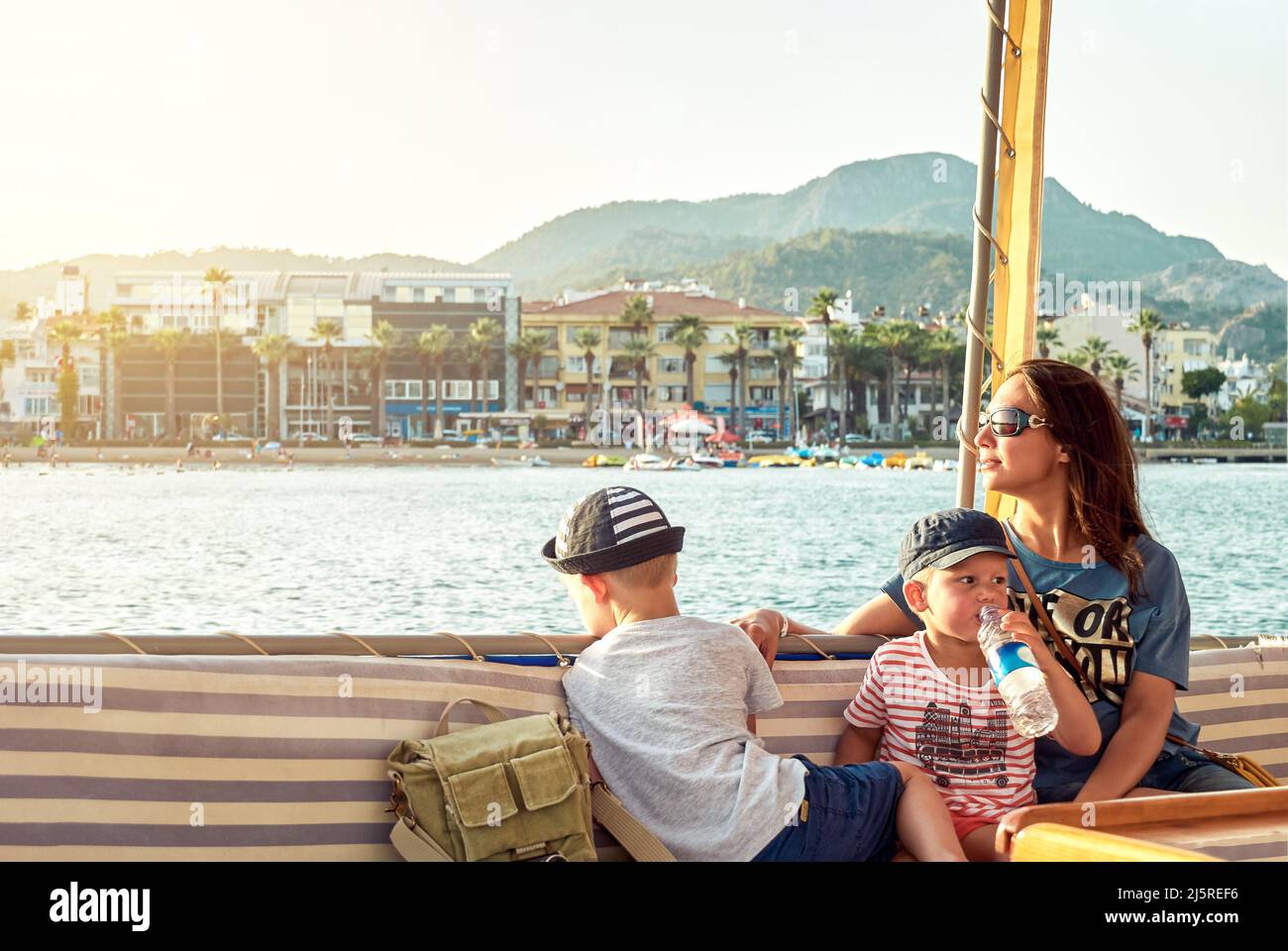 Mutter und Söhne entspannen sich auf einem Boot, das im Meer entlang der Küste von Marmaris gegen Berge segelt. Frau mit Kleinkind und Vorschulkinder genießen Urlaub in Turk Stockfoto