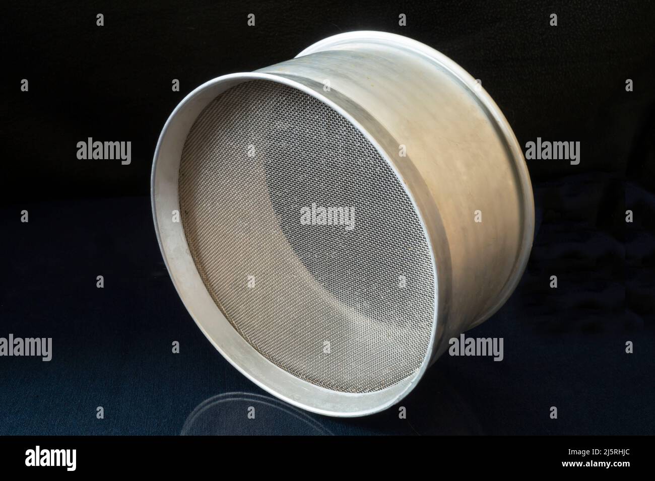 Ein Metallmehlsieb auf dem Küchentisch. Küchenutensilien auf schwarzem Hintergrund Stockfoto