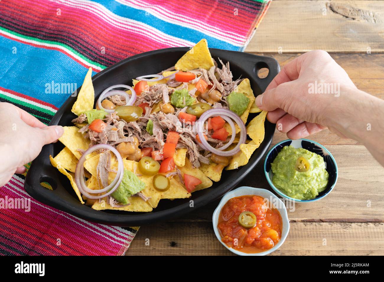 Hände, die Nahrung aus einem Tablett Nachos mit Fleisch nehmen. Schüsseln mit Salsa. Speicherplatz kopieren. Mexikanisches Küchenkonzept. Stockfoto