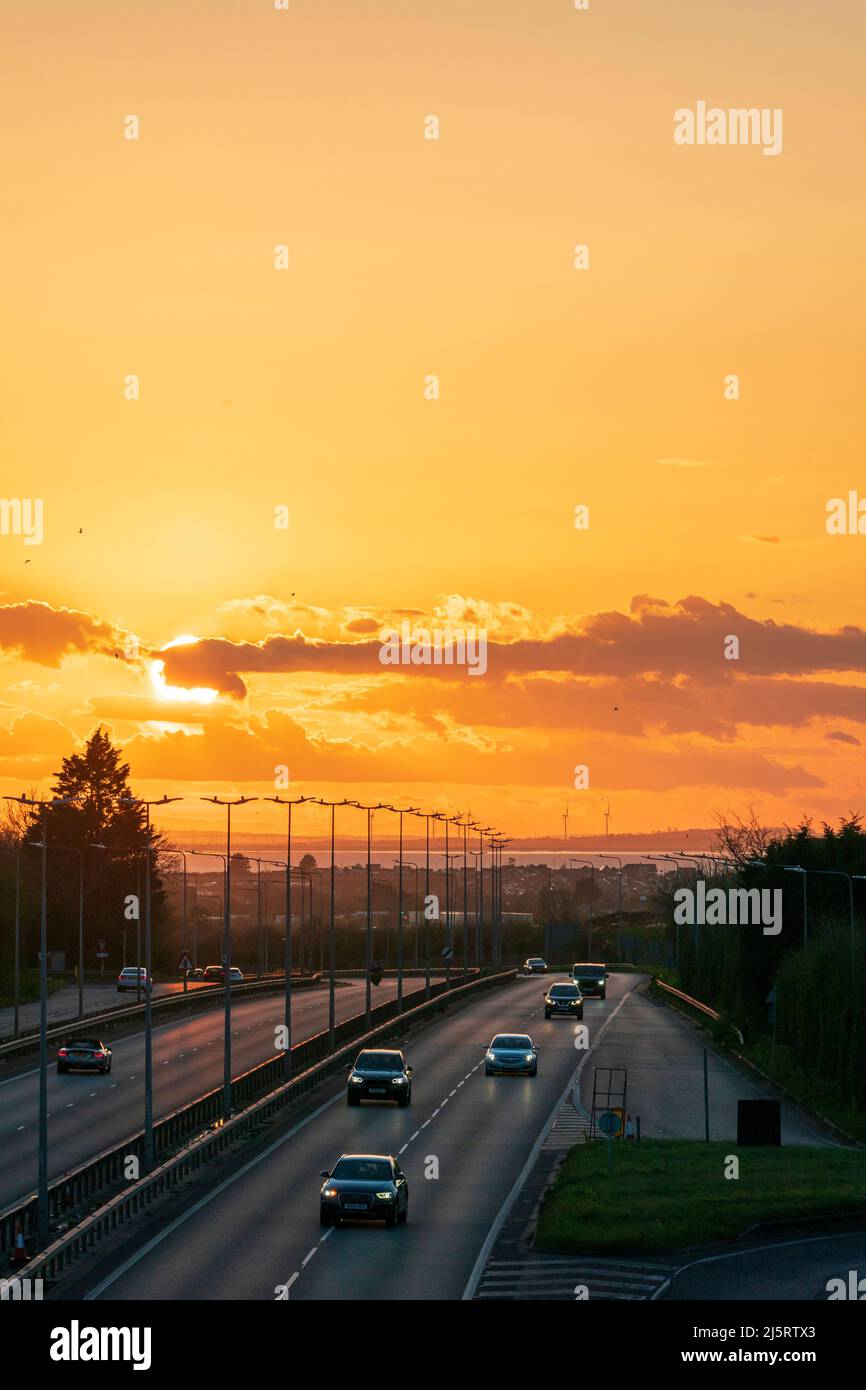 Sonnenuntergang in einem wolkig-orangenen Himmel über der A299, Thanet Way Doppelspurstraße mit der Isle of Sheppey im Hintergrund und Windfarmturbinen. Teleaufnahmen. Stockfoto