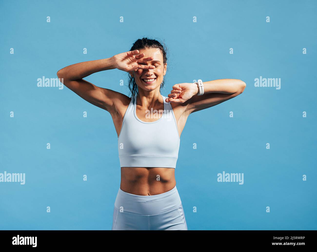 Glückliche Fitness-Frau, die sich nach dem Training entspannt. Junge Frauen im Sport tragen ein verstecktes Gesicht mit Händen auf blauem Hintergrund. Stockfoto