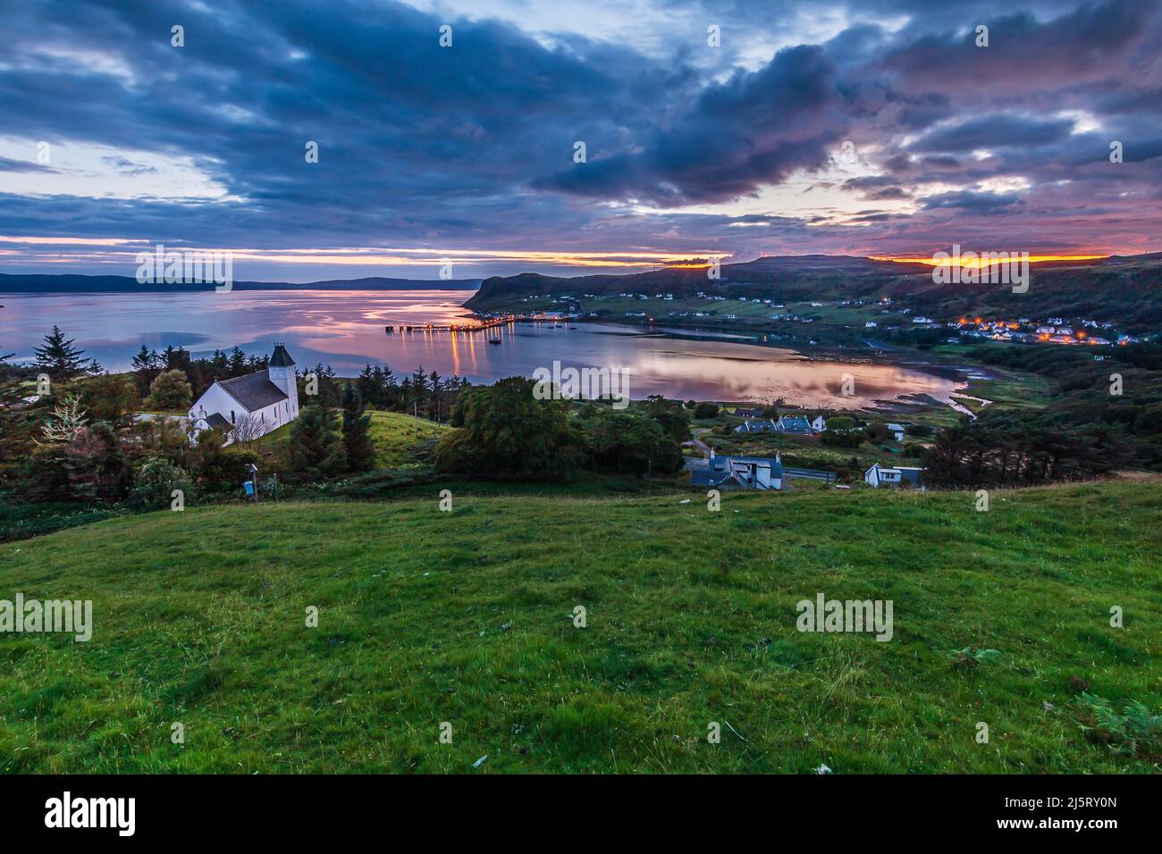 Panorama der Isle of Skye am Abend. Kleine Stadt Uig in Schottland im Sommer. Abendstimmung bei Sonnenuntergang. Kirche und andere Gebäude auf einem Hügel in Stockfoto
