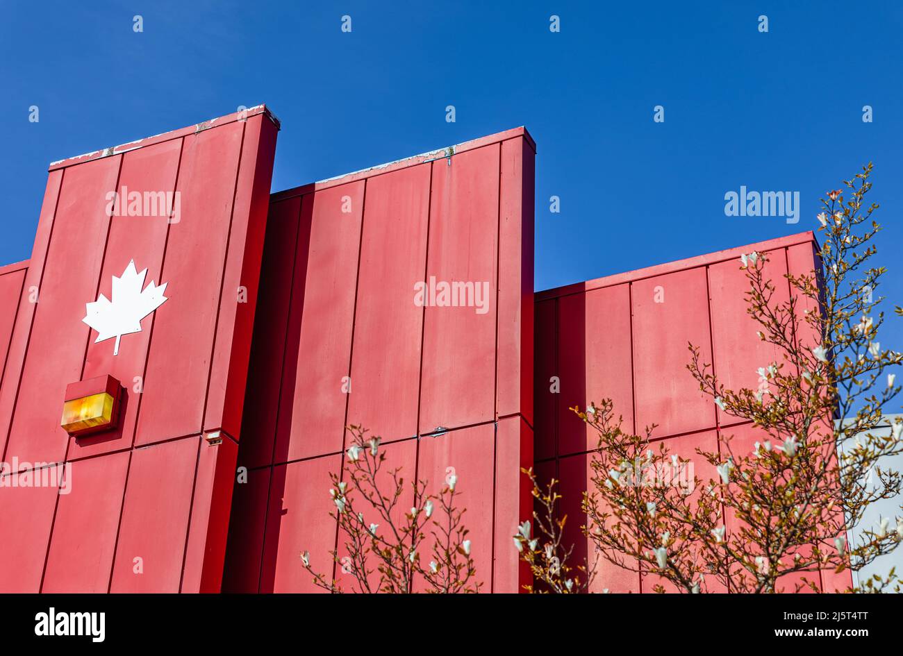 Die Wand des Gebäudes mit dreieckigen Projektionen. Moderne Architektur in roter Farbe in Kanada. Abstraktes Gebäude mit geometrischem Muster und Frühlingsbaum Stockfoto