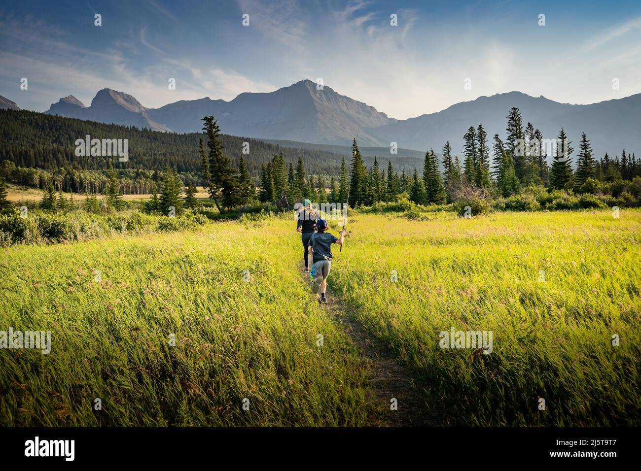 Zwei Kinder, die im Sommer in den kanadischen Rockies in der Nähe des Crowsnest Pass Alberta Canada einen Pfad über eine Wiese mit Angelruten entlang laufen Stockfoto