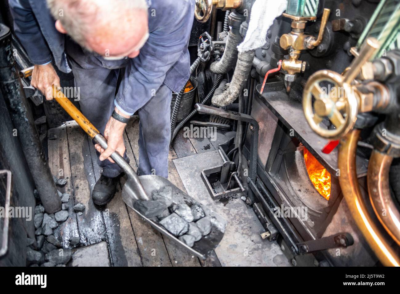 Kohle wird in die Feuerstelle einer Dampflokomotive geschaufelt. Ingenieur, Fahrer, Feuerwehrmann in der Kabine von Hunslet Sparity 0-6-0 Fütterung Kohle Brennkessel Stockfoto