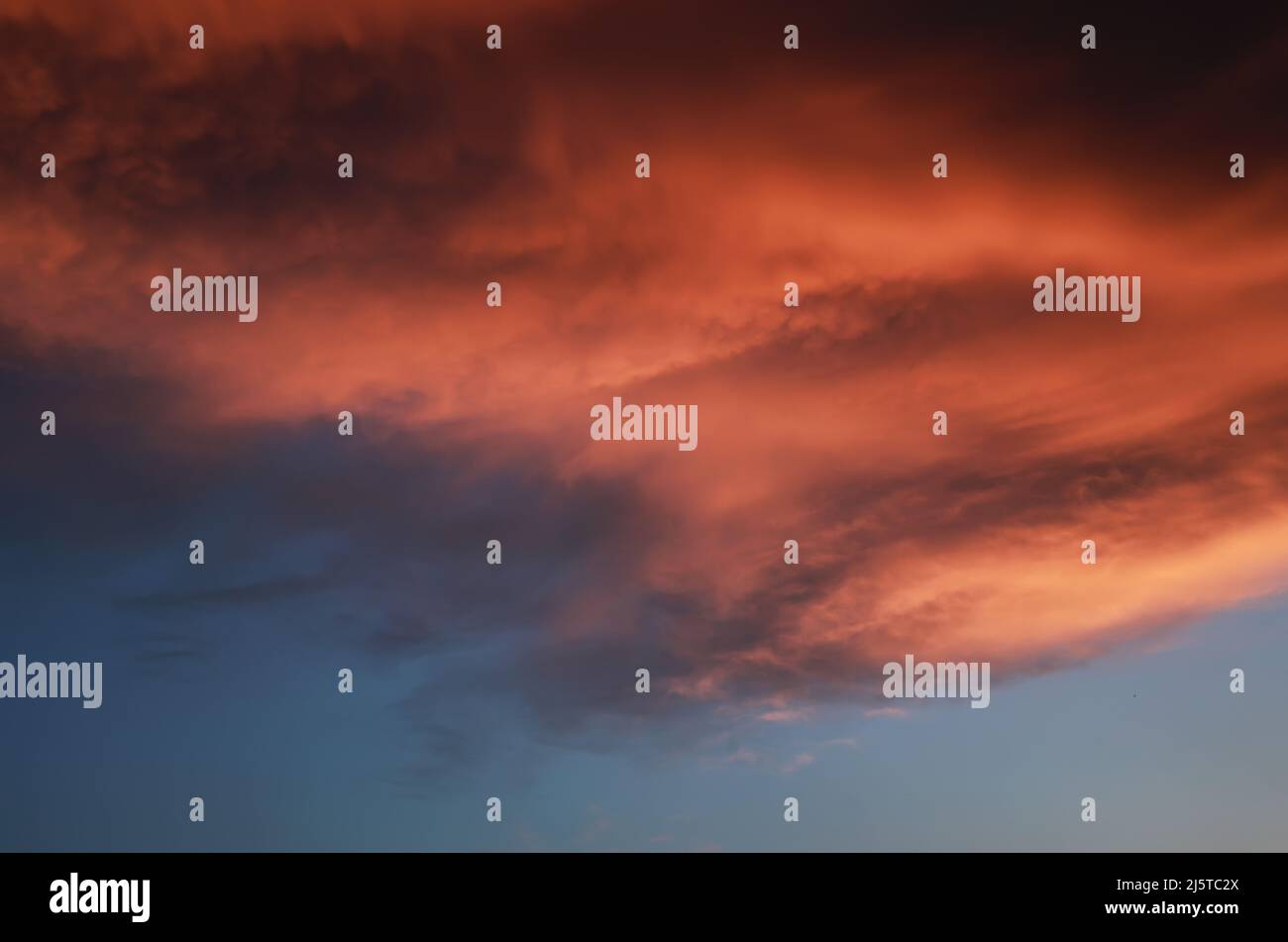 Dramatische Sonnenuntergangslandschaft mit geschwollenen Wolken, die von der orangefarbenen untergehenden Sonne und dem blauen Himmel beleuchtet werden Stockfoto