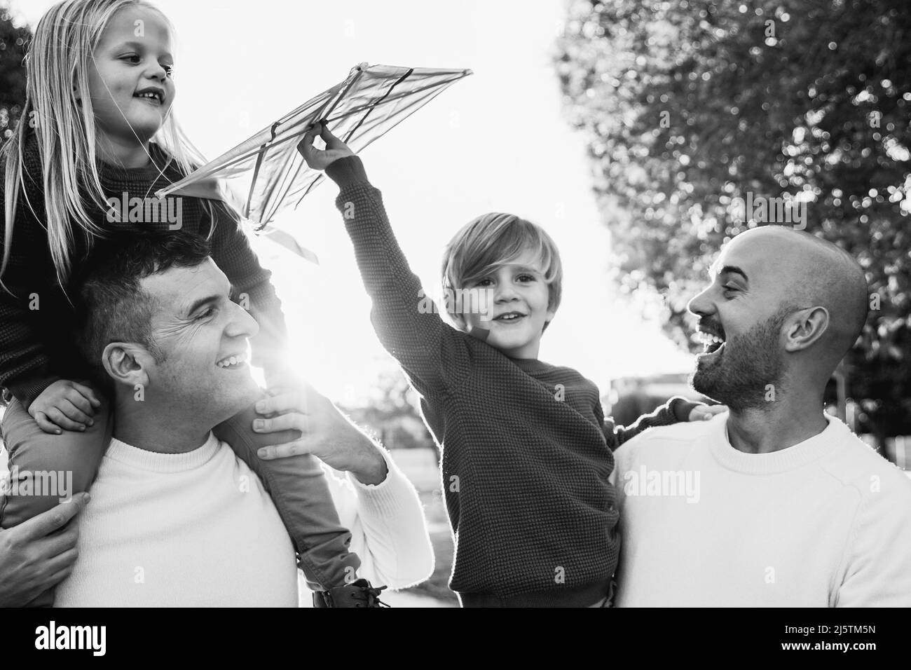 Schwule männliche Paare und Kinder, die Spaß mit Drachenspielzeug im Freien haben - LGBT-Familie und Liebeskonzept - Fokus auf linkes Vatergesicht - Schwarz-Weiß-Schnitt Stockfoto