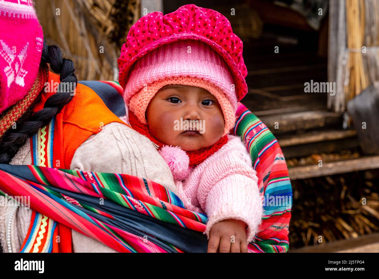 Ein Uros-Baby wird in Einem Sling auf den schwimmenden Uros-Inseln, dem Titicacasee, Puno, Peru, getragen. Stockfoto