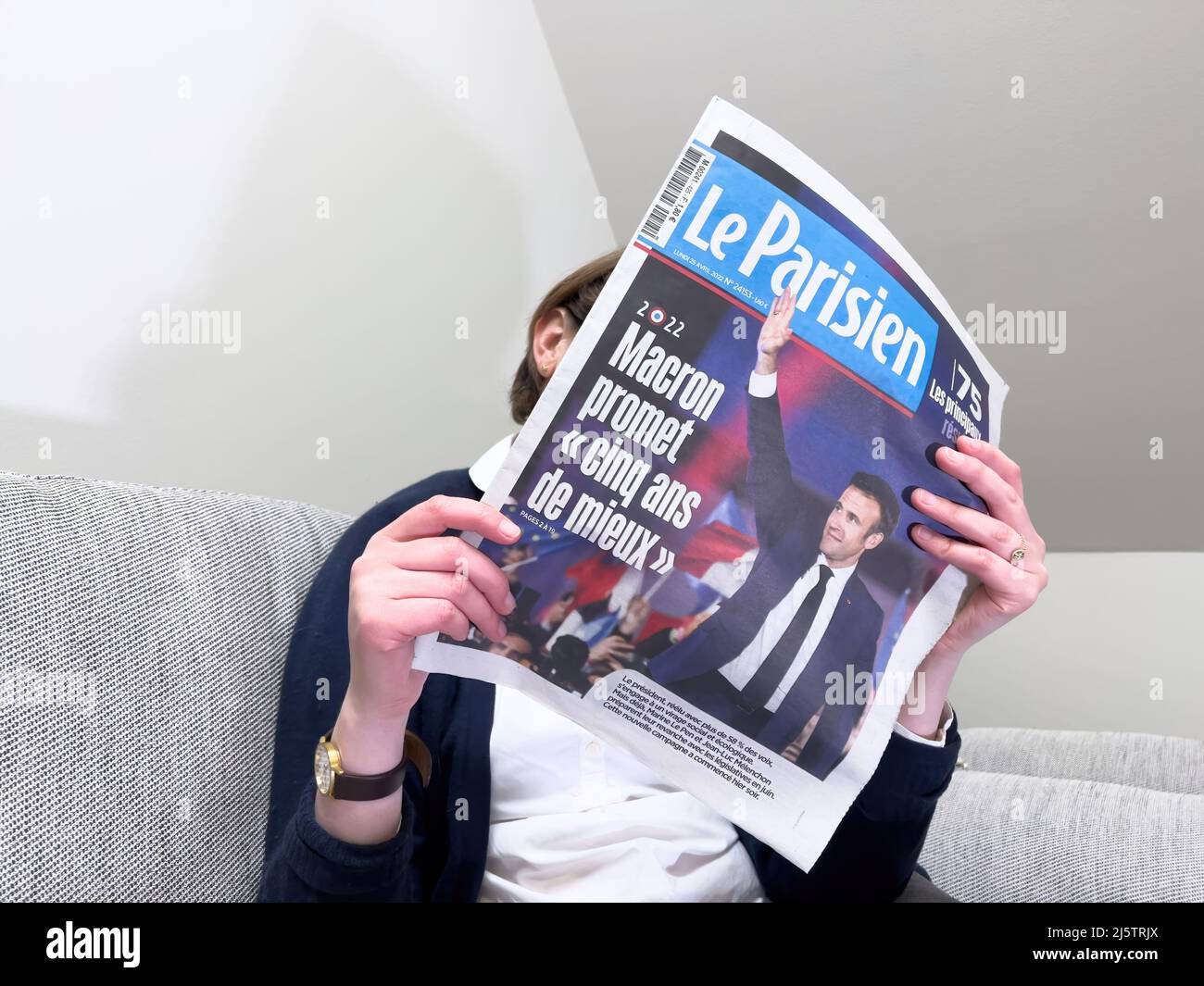 Paris, Frankreich - 25. Apr 2022: Frau liest auf einer gemütlichen Couch die neueste ZEITUNG LE Parisien berichtet über Frankreichs amtierender Präsident Emmanuel Macron, nachdem er Marine Le Pen für eine zweite fünfjährige Amtszeit geschlagen hatte Stockfoto