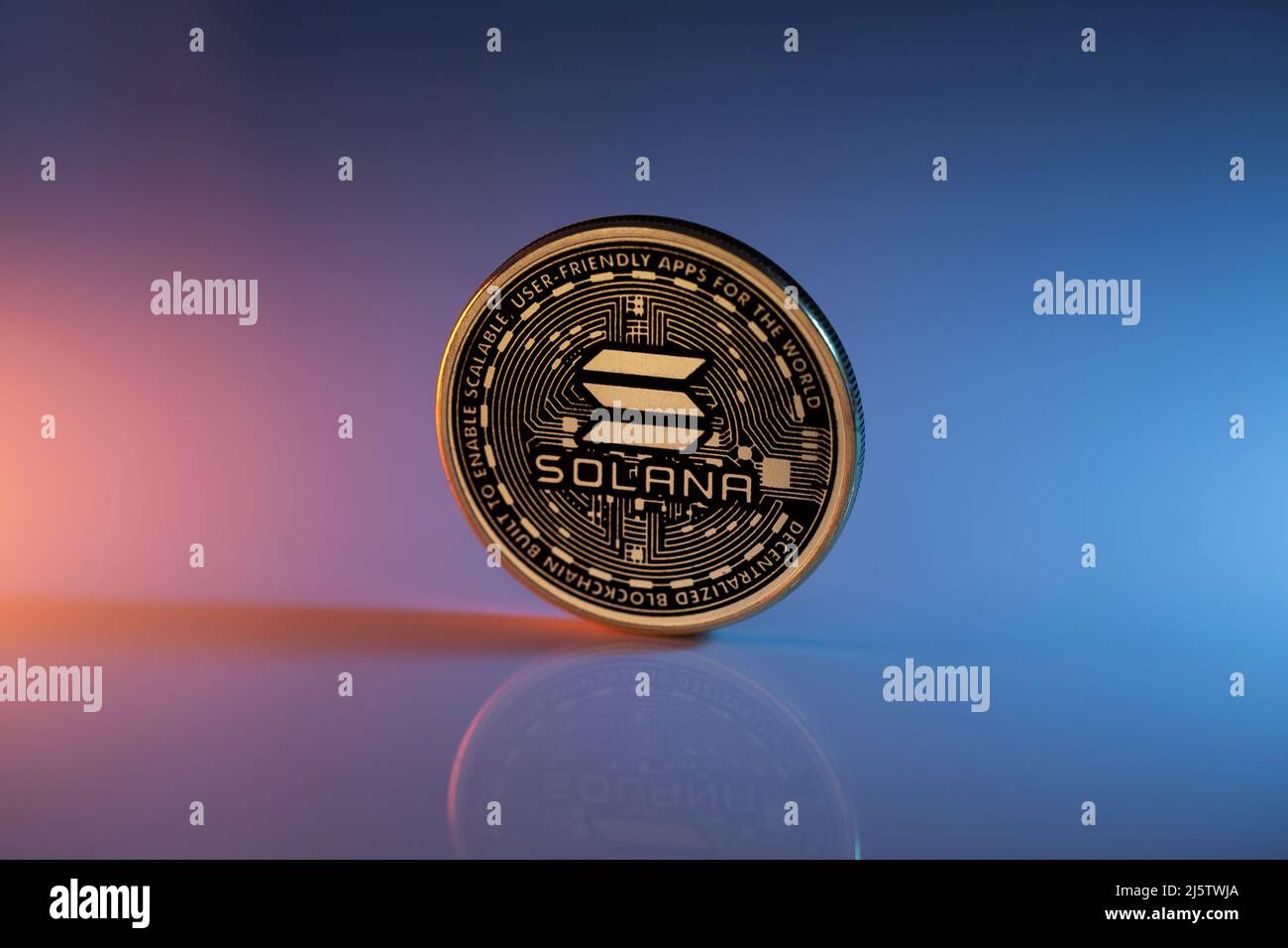 Solana SOL Kryptowährung physische Münze auf reflektierender Oberfläche platziert und mit orangefarbenen und blauen Lichtern beleuchtet. Makroaufnahme. Selektiver Fokus. Stockfoto