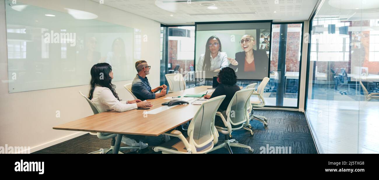 Moderne Geschäftsleute, die in einem Sitzungssaal eine Videokonferenz abhalten. Gruppe kreativer Kollegen, die an einem virtuellen Briefing mit ihren Partnern teilnehmen. Global Stockfoto