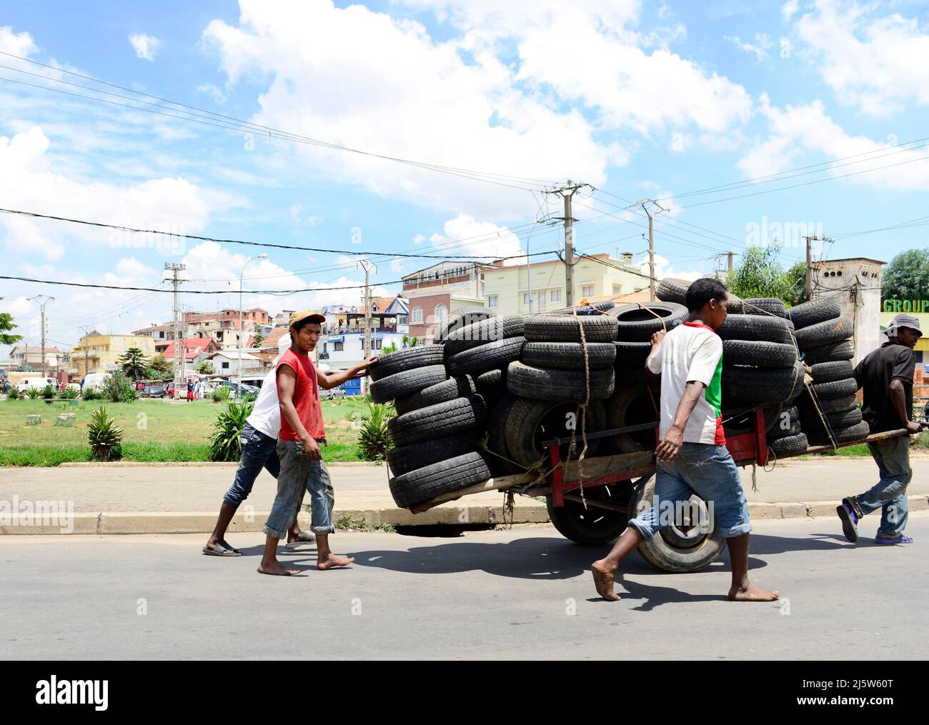 Eine Gruppe madagassischer Männer, die in den Vororten von Antananarivo, Madagaskar, einen Wagen voller Reifen ziehen. Stockfoto