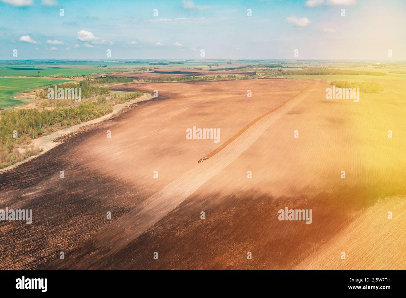 Luftaufnahme, Draufsicht Traktor-Pflügefeld in der Frühjahrssaison. Beginn Der Frühjahrssaison Für Die Landwirtschaft. Grubber, der von Einem Traktor auf dem Land gezogen wird Stockfoto