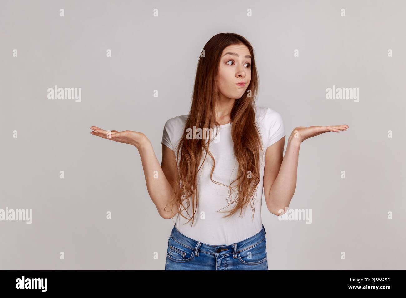 Weiß keine Antwort. Porträt von lustig verwirrt Mädchen zuckend Schultern mit ahnungslos peinlich Ausdruck, Zweifel, trägt weiße T-Shirt. Innenaufnahme des Studios isoliert auf grauem Hintergrund. Stockfoto