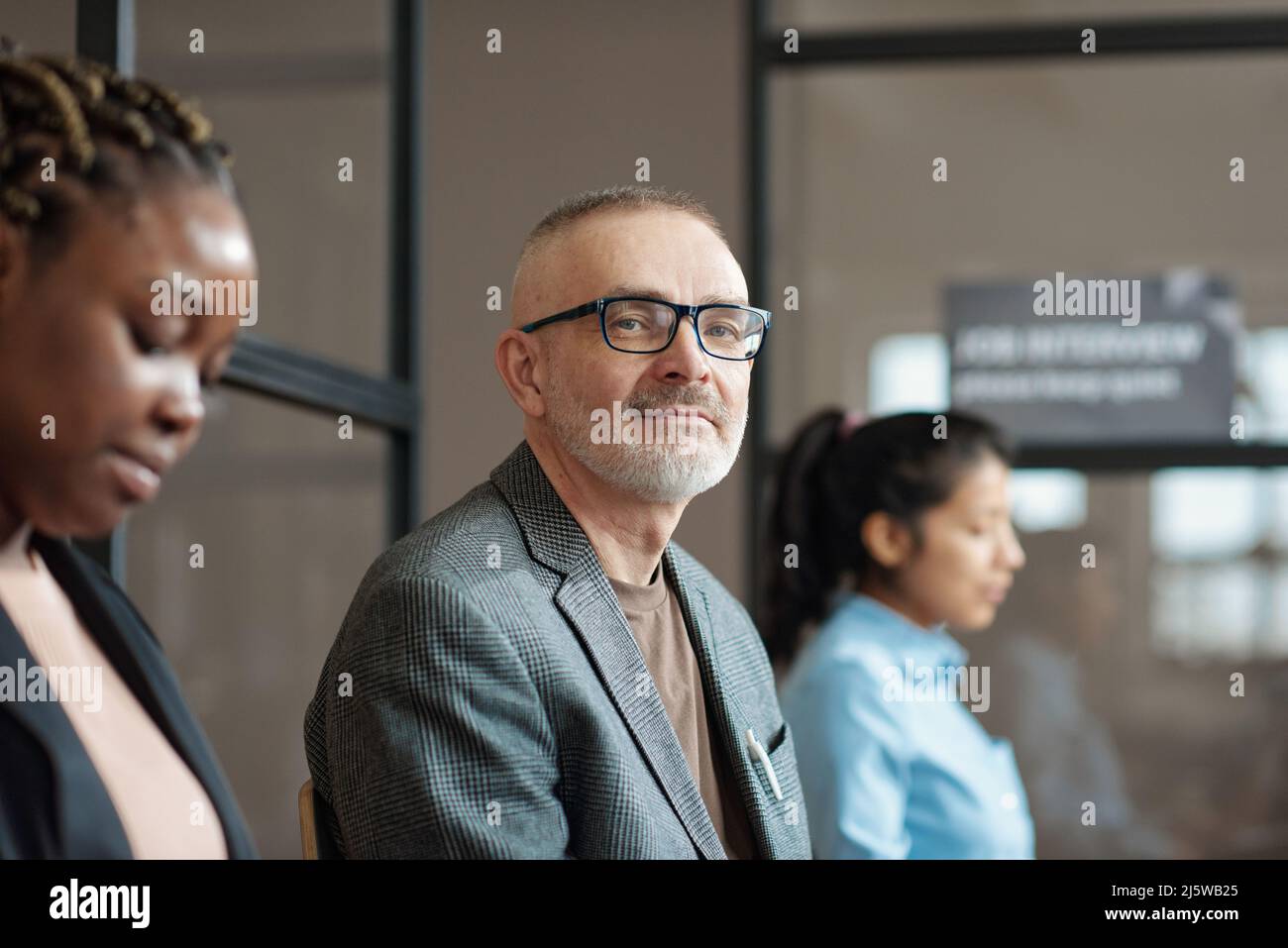 Porträt eines reifen Mannes in einer Brille, der die Kamera anschaut, während er im Wartezimmer des Büros sitzt Stockfoto