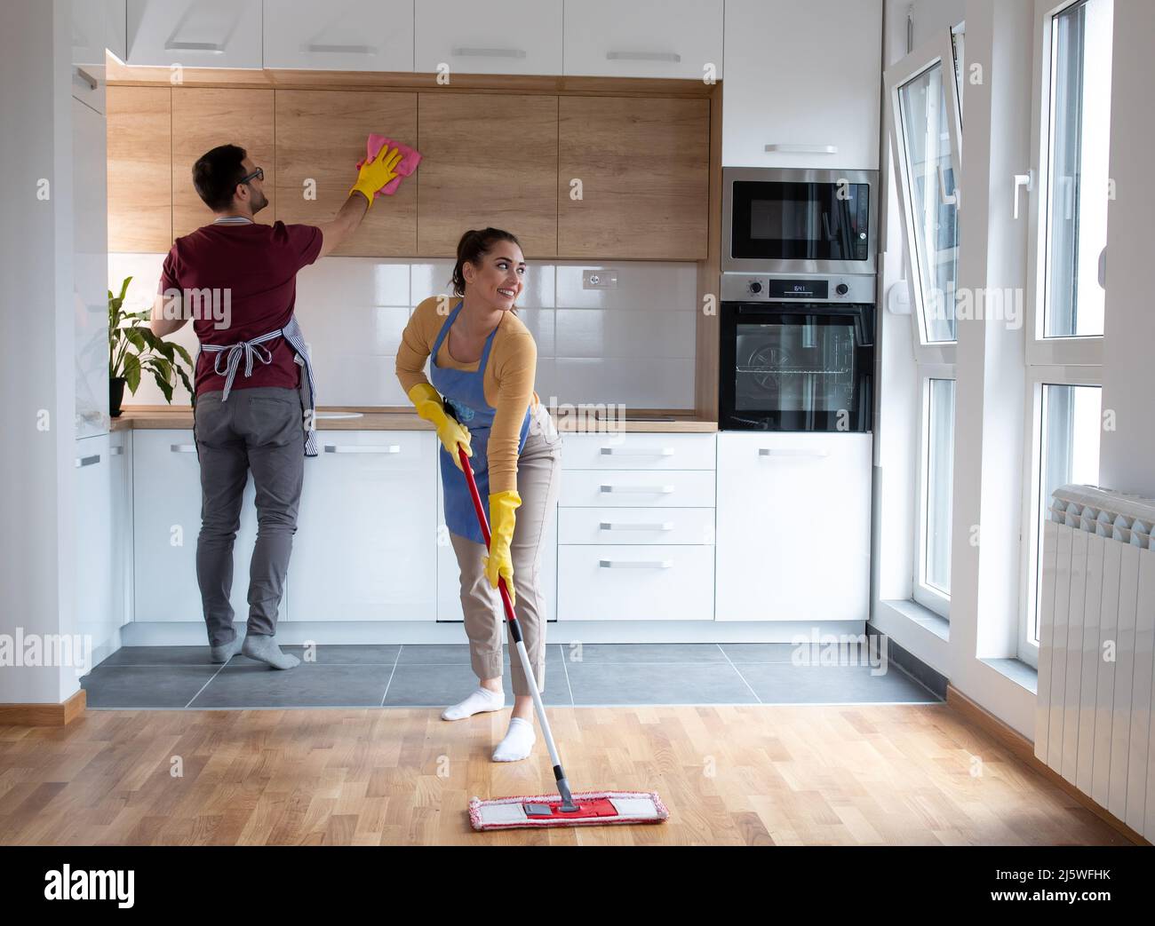 Ehepaar macht gemeinsam Hausarbeiten, während junge Frau mit einem Wischmann den Staub aus der Küche in ihrer Wohnung wischt. Stockfoto