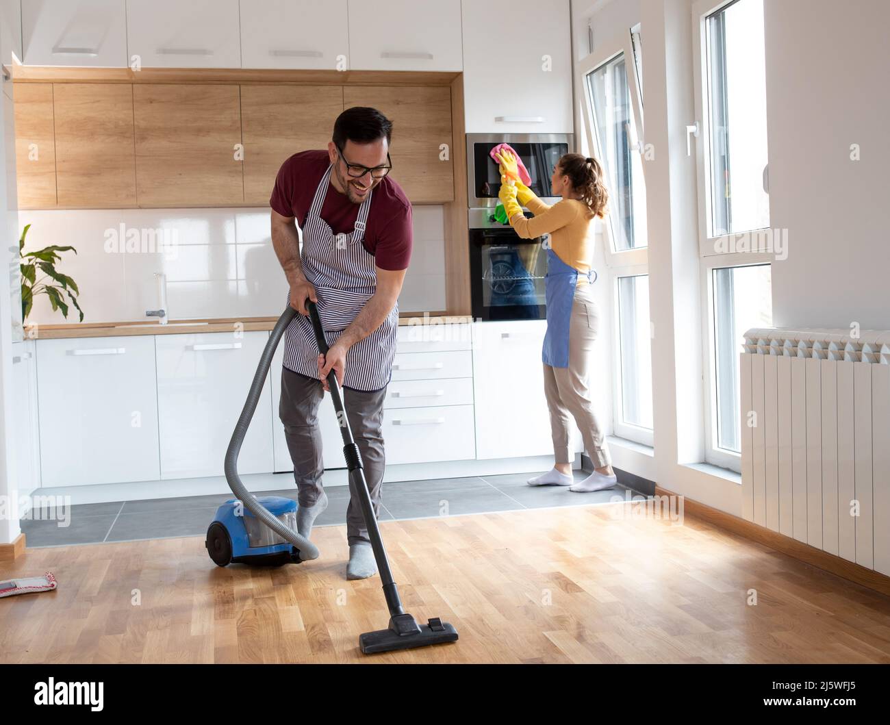 Das Paar erledigt ihre Arbeit zusammen, während eine Frau den Staub abwischt und ein Mann den Boden mit einem Staubsauger saugt. Stockfoto