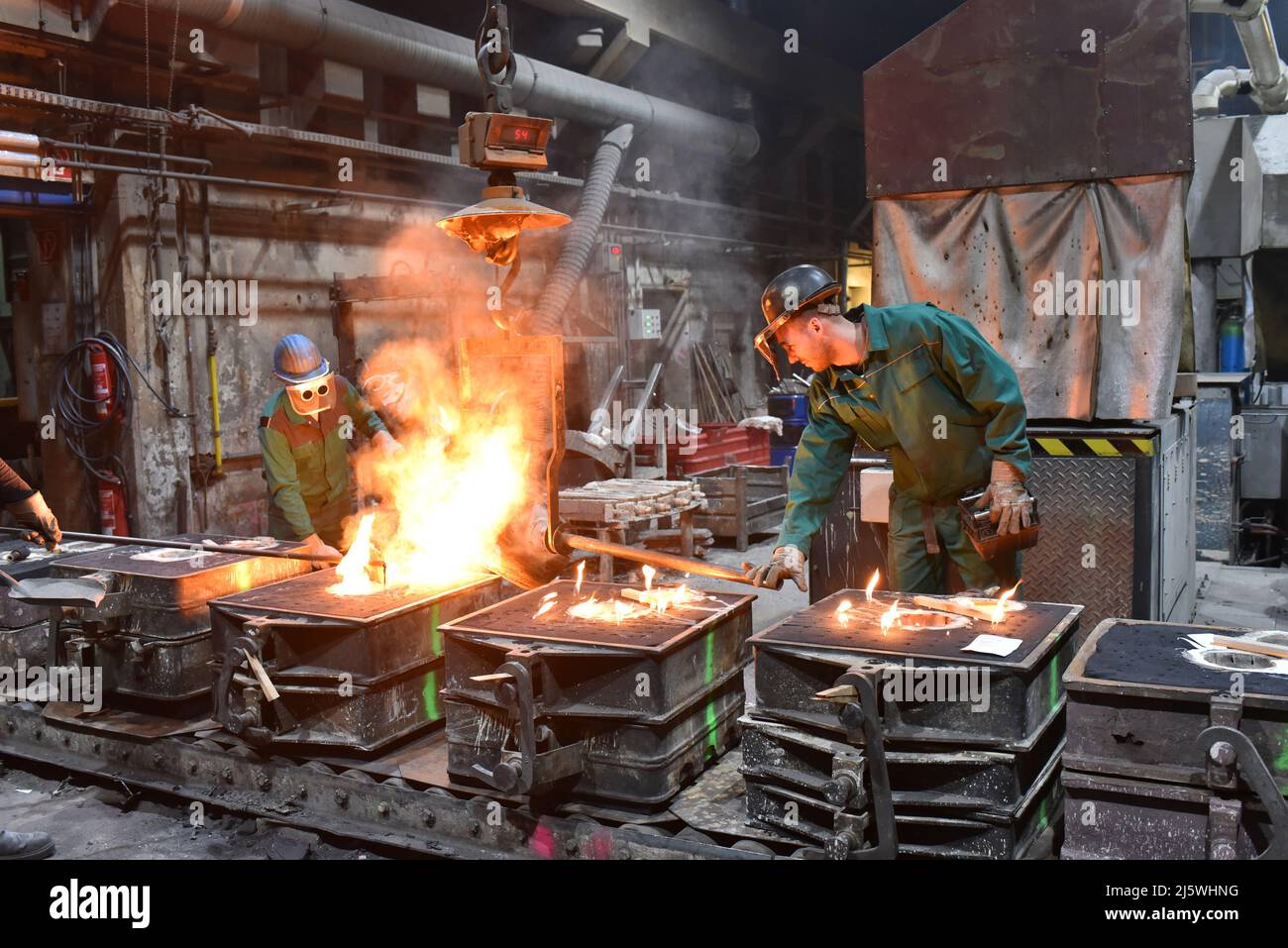 Die Arbeiter in der Gießerei, die das metallische Werkstück gießen - Sicherheit bei der Arbeit und Teamarbeit - Nahaufnahme prhoto Stockfoto