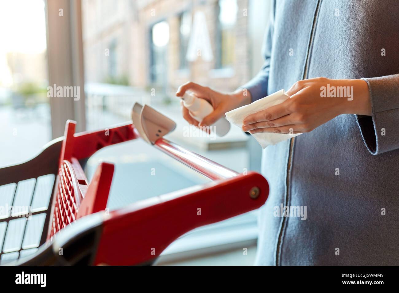 Frau, die den Griff des Warenkorbs mit Desinfektionsmittel reinigt Stockfoto