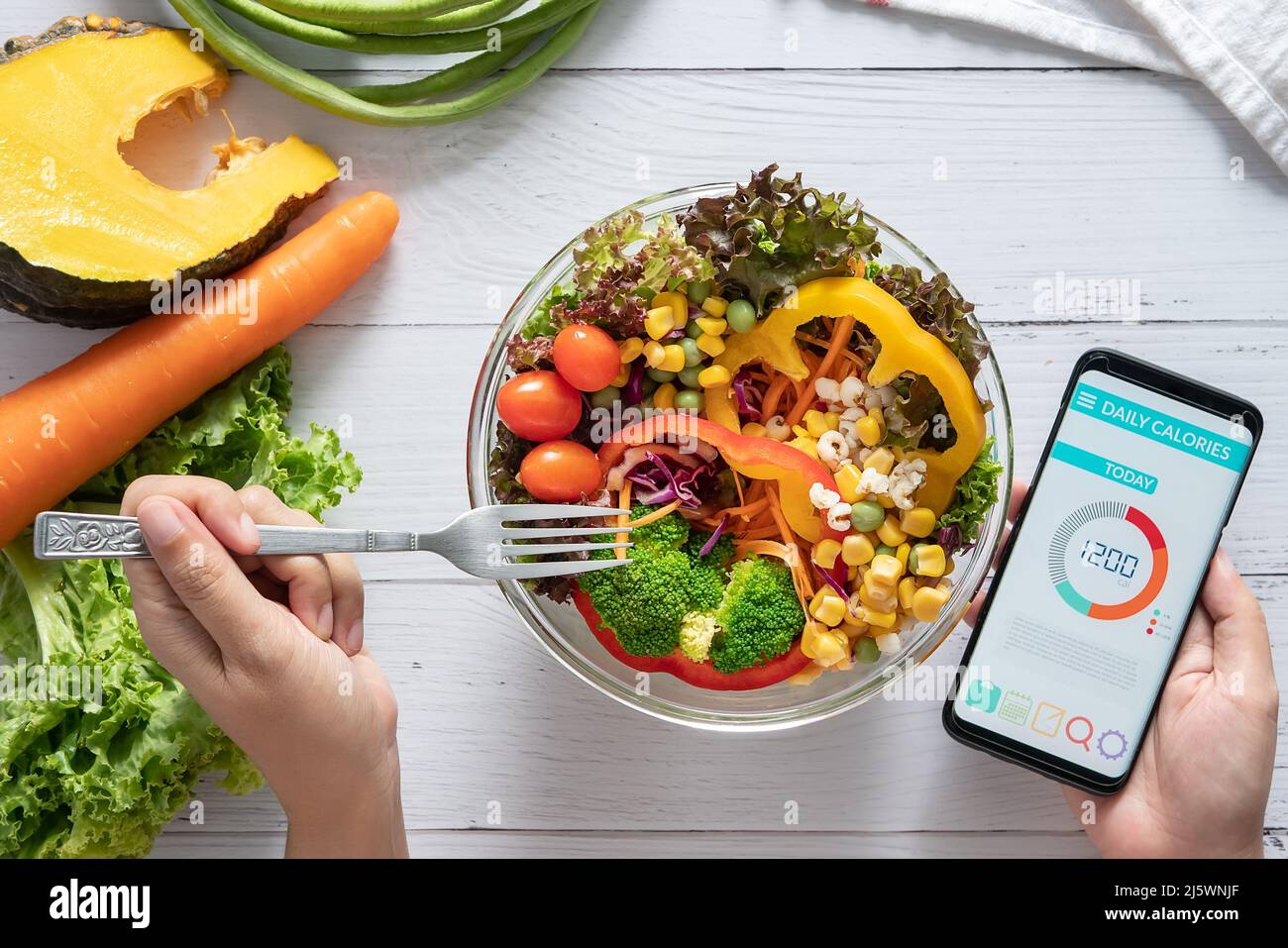 Kalorienzählen, Ernährung, Kontrolle der Lebensmittel und Gewichtsverlust Konzept. Kalorienzähler Anwendung auf Smartphone-Bildschirm am Esstisch mit Salat, Obst Stockfoto