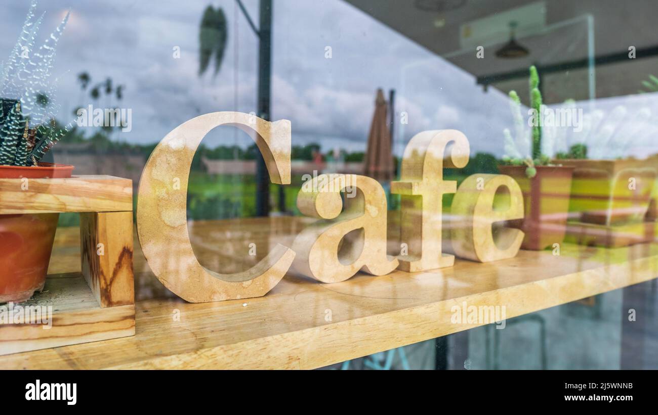 Holzschild für das Café hinter einem großen Glasfenster, das den Blick vor dem Café im Hintergrund reflektiert Stockfoto