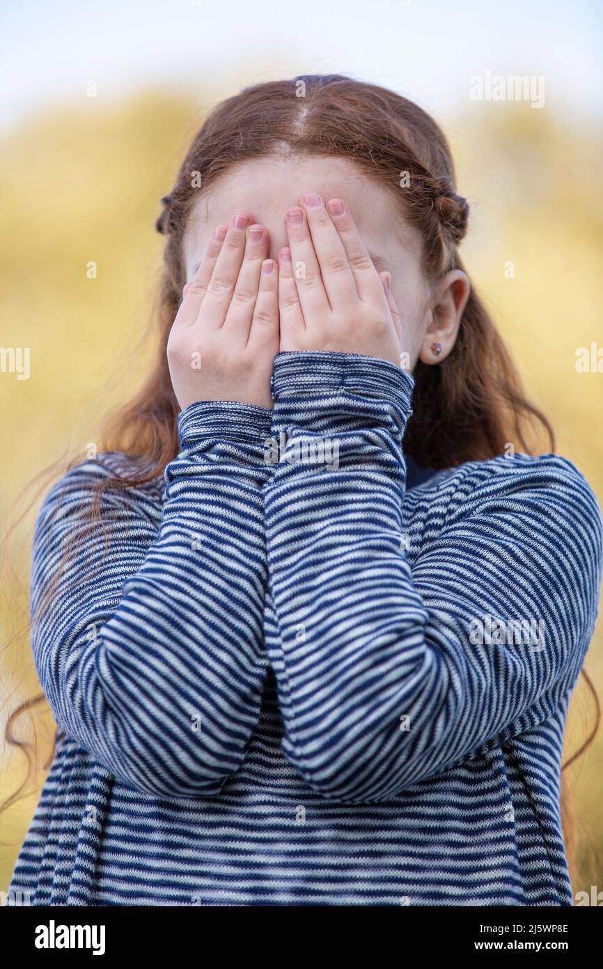 Verängstigte Rotschopf-Mädchen, die sich mit Händen im Gesicht verstecken Stockfoto