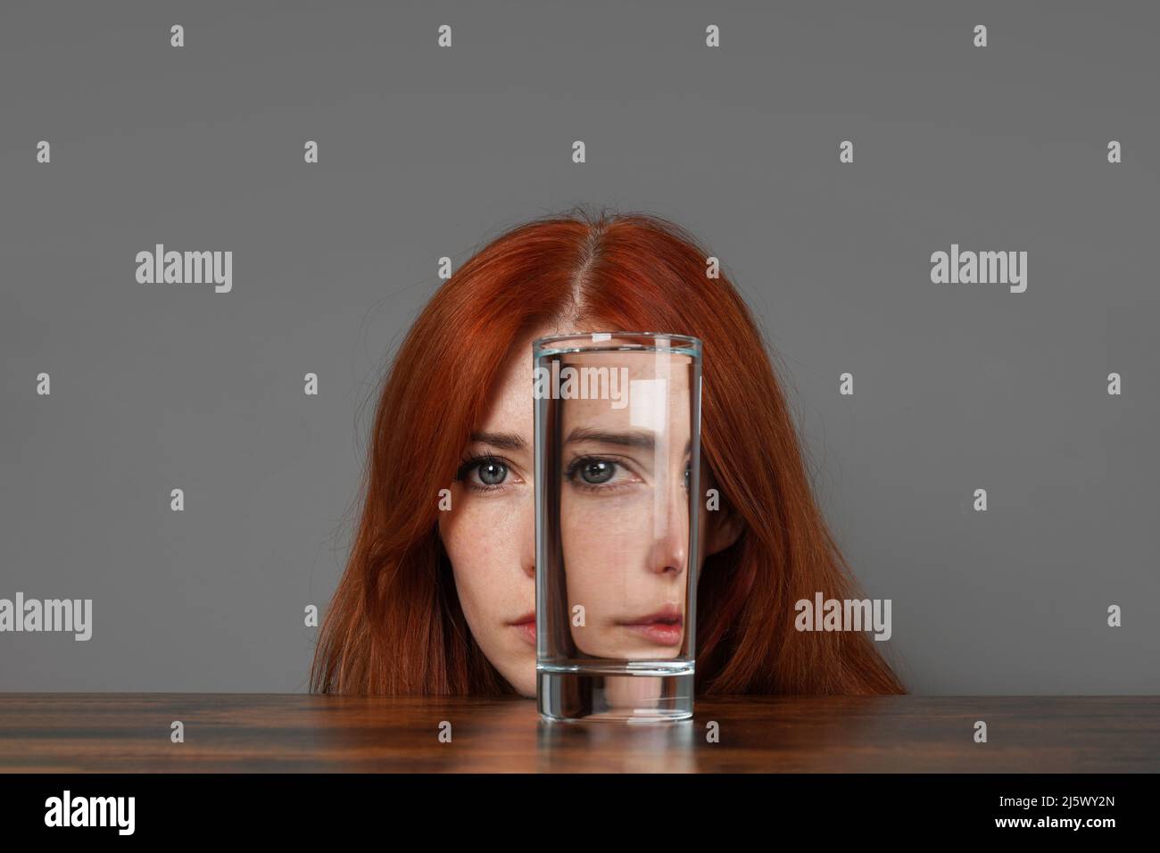 Verzerrtes Gesicht einer Frau, die durch ein Glas Wasser schaut Stockfoto