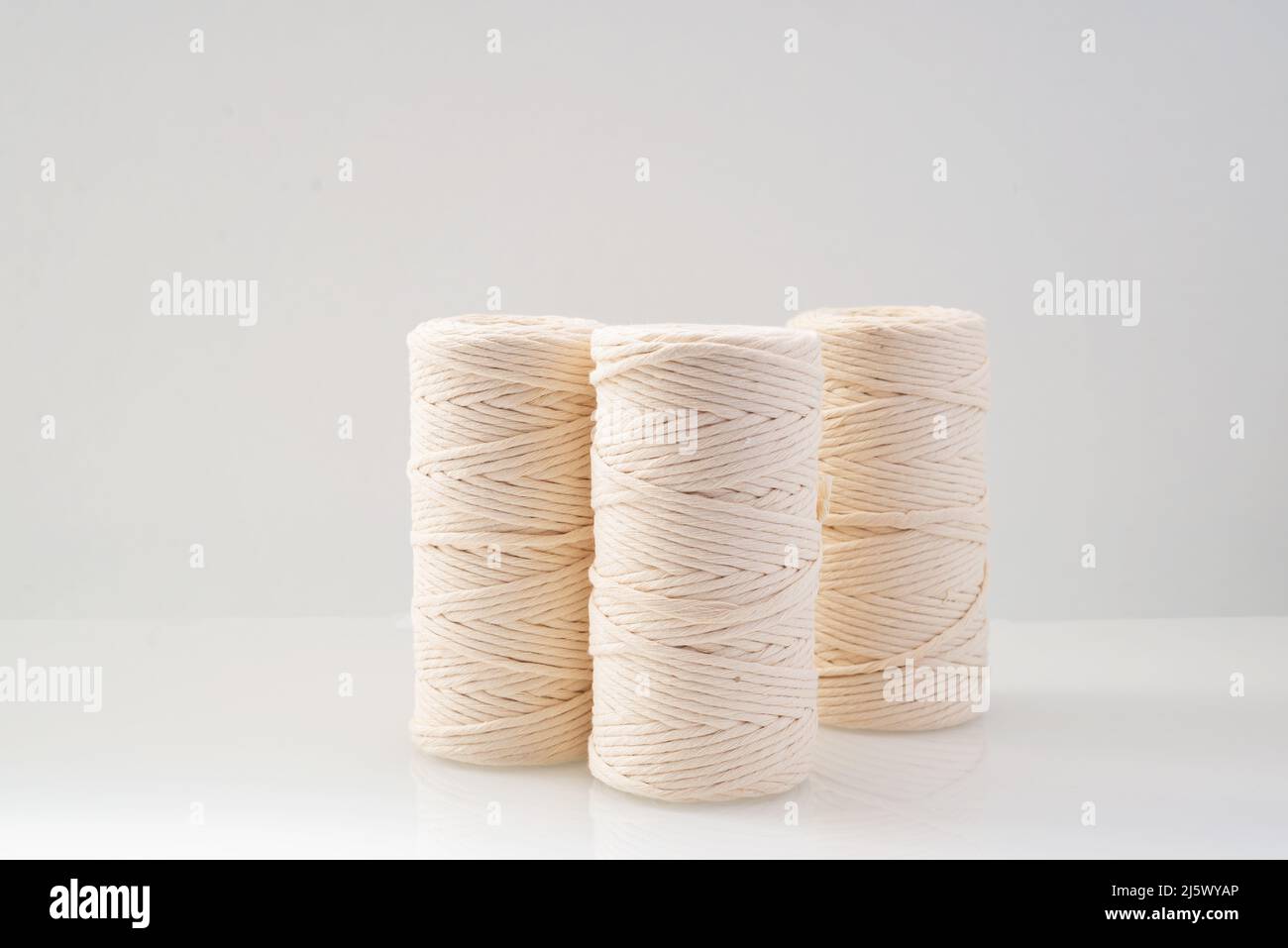 Makramfäden aufgewickelte Spulen in natürlicher beiger Farbe befinden sich auf einem hellen Hintergrund Stockfoto